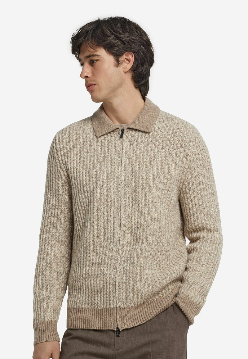 Beige ribbad stickad cardigan med dragkedja och en kontrasterande krage. Har texturerad tyg och en figursydd midjedetalj.