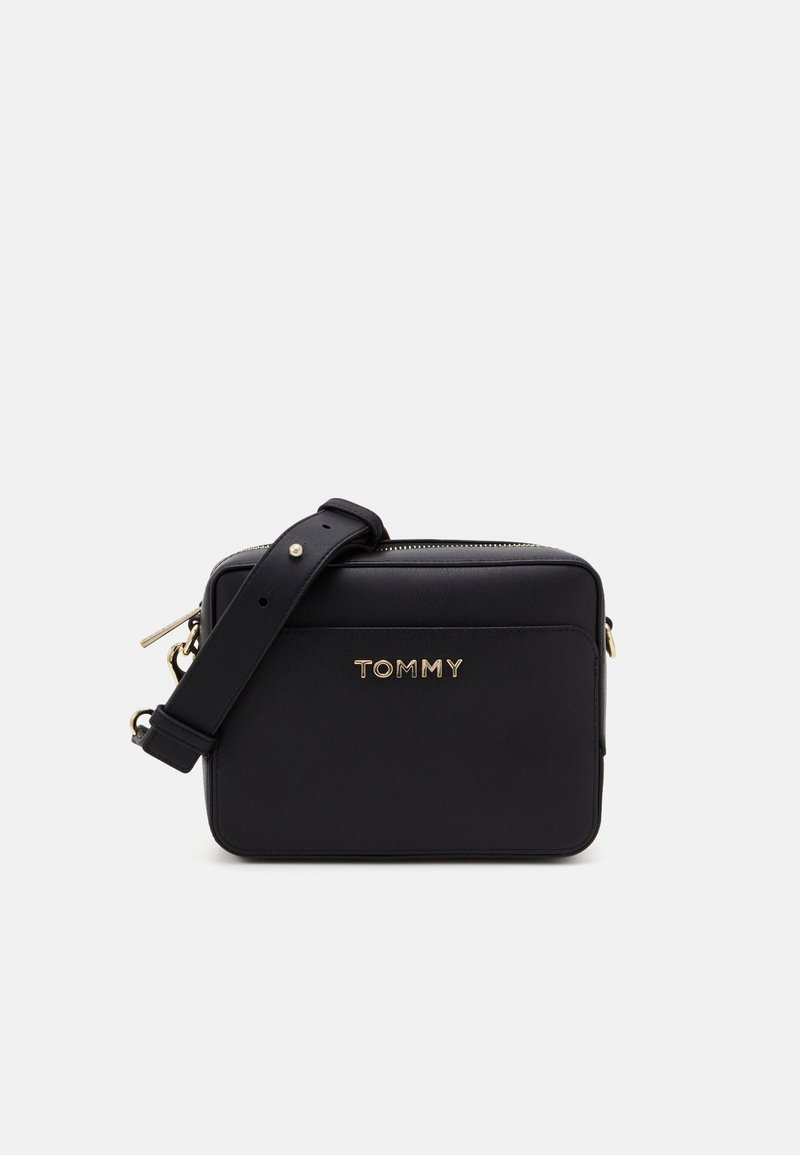 Czarna syntetyczna torebka na ramię w prostokątnym kształcie, z złotym logo "TOMMY", zamknięciem na zamek błyskawiczny i regulowanym paskiem. Gładka faktura na całej powierzchni.