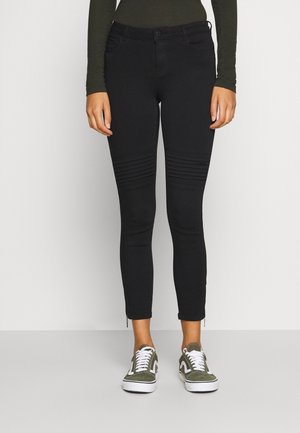Pantalones negros ajustados con detalles acanalados en las rodillas, elaborados con una tela elástica, combinados con zapatillas verde y blancas.