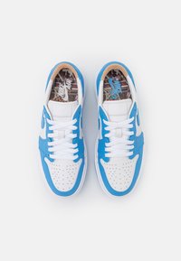 Paire de baskets Nike Air basses blanches et bleues avec lacets blancs, bout perforé et semelles intérieures à motifs, vues de dessus.