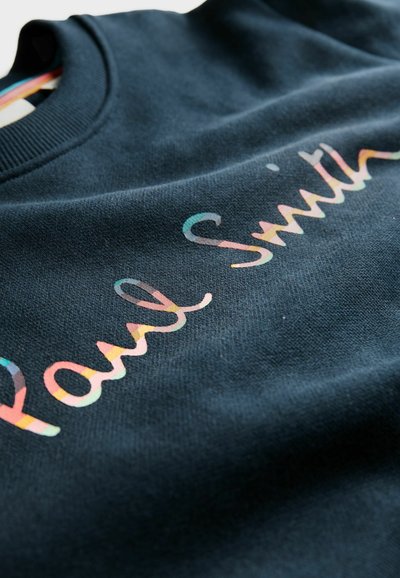 Tmavomodrá mikina s mäkkou textúrou, na prednej strane s farebným logom "Paul Smith" v hravej kurzívnej typografii.