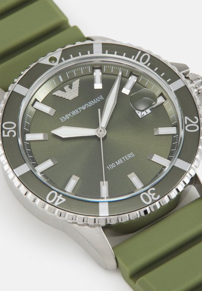 Montre avec bracelet en silicone vert, boîtier en acier inoxydable, cadran vert, index horaires argentés et guichet de date à 3 heures. Résistante à l'eau jusqu'à 100 mètres.