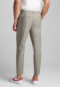 Szare lniane spodnie o eleganckim, zwężanym kroju, z elastyczną talią i dwiema tylnymi kieszeniami, w połączeniu z białymi i czerwonymi trampkami.