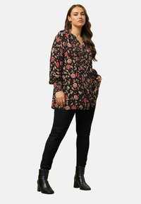 Tunic nera con fiori rossi e beige, maniche lunghe, scollatura a V e tasche, abbinata a jeans skinny neri e stivali alla caviglia.