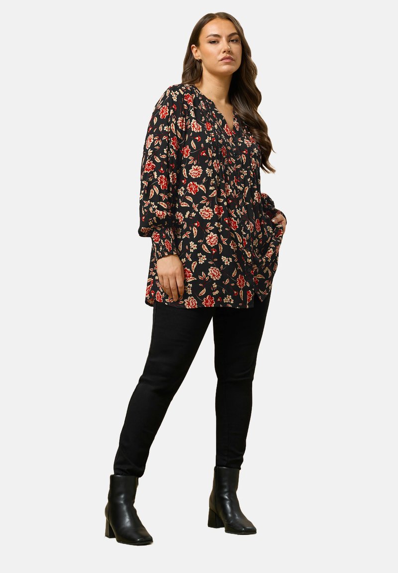 Tunic nera con fiori rossi e beige, maniche lunghe, scollatura a V e tasche, abbinata a jeans skinny neri e stivali alla caviglia.