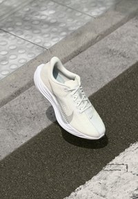 Letvægt løbesko i off-white, med en struktureret mesh-overdel, forstærket hæl og fleksibel sål. Nike-logo på siden.