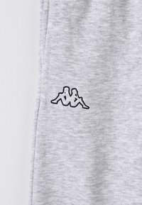 Grått tyg med en svart broderad logotyp som föreställer två sittande, rygg mot rygg mänskliga silhuetter på vänster sida.