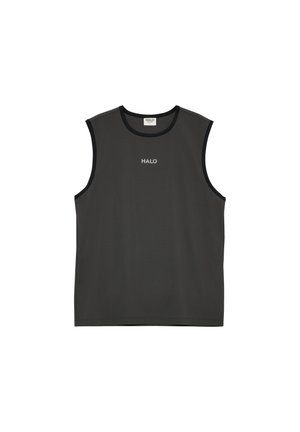 Voksen mand står iført sort ærmeløs skjorte, sorte lagdelte shorts over grå kompressionsshorts, hvide sokker og grå sneakers.