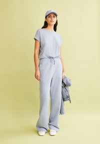 Top grigio chiaro a maniche corte con vestibilità rilassata; pantaloni abbinati a vestibilità ampia con cordoncino; abbinati a scarpe bianche e giacca di jeans.