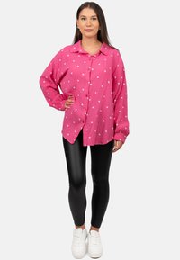 Camicia rosa a maniche lunghe con motivo a cuori bianche, dal fit rilassato, abbinata a leggings neri e sneakers bianche.
