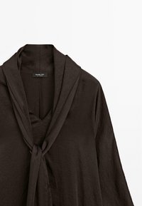 Maglioncino marrone scuro realizzato in un tessuto morbido e strutturato, con scollatura a V e un colletto drappeggiato legato davanti. Etichetta del marchio visibile nel collo.