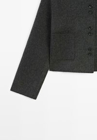 Mroczna szara wełniana kurtka, ukazująca rękaw i dolną część z pięcioma guzikami oraz kwadratową kieszenią z przodu na białym tle.