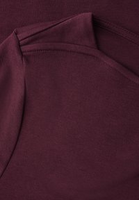 Detailaufnahme von gefalteten Nahtdetails auf einem dunkelvioletten Strickstoff, die die Textur und die Nähte betont.