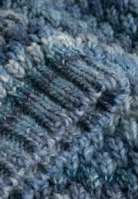 Nærbillede af blødt, tykt blå garn strikket i et tekstureret, ribbet mønster med varierende nuancer af blå og grå.