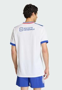 Bílý sportovní dres s modrými akcenty a červeným lemováním. Na zadní straně je logo označené "SOCIETE GENERALE", vyrobené ze syntetického materiálu.