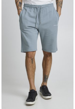 Light blue cotton shorts with an elastic waistband and drawstring. Side pockets and a printed logo on the lower front.