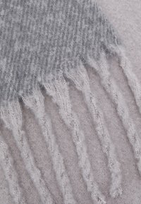 Harmaa ja vaaleanharmaa villasekoitekangas, jossa on houndstooth-kuvio ja fringe-yksityiskohtia reunoilla. Pehmeä rakenne.