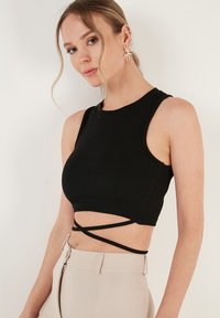 Must mustriba crop top kõrge kaelusega ja ilma varrukateta, millel on ristuvad rihmad vööl, et saavutada kehakujuline välimus.