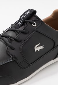 Black leather sneaker with lace-up design, perforated detailing, and a contrasting white rubber sole. Features silver logo on the side.