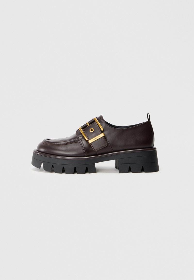 Brown leather shoe with a chunky black sole, features a large gold buckle and smooth texture, designed with a rounded toe.
