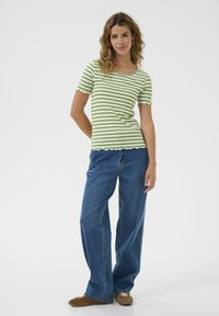 Grün-weiß gestreiftes, geripptes T-Shirt mit wellenförmigem Ausschnitt und kurzen Ärmeln, kombiniert mit hellblauen Jeans mit weitem Bein.