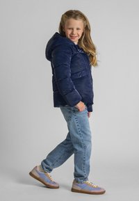 Tumesinine puffjakker kapuutsiga, millel on k杀 feito kuue oma. Kantud heledate siniste teksade ja mitmevärviliste madalate spordijalatsitega.