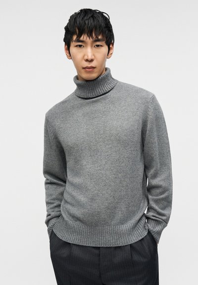 Γκρι πουλόβερ με ζιβάγκο σε απαλό, υφασμένο πλεκτό ύφασμα με ριμπ λαιμόκοψη και τελείωμα, σε συνδυασμό με σκούρο παντελόνι με κάθετες ρίγες.