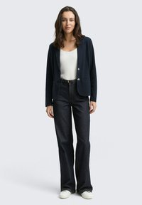 Navy blazer with two buttons over a white top, paired with dark flared jeans and white sneakers. Smooth fabric with tailored design.