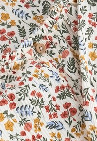 Stof met bloemenpatroon met kleine rode, gele, blauwe en groene bloemen op een witte achtergrond. Gelaagd katoen met een knoopdetail.