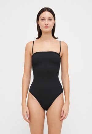 Black one-piece swimsuit with thin straps, textured fabric, and square neckline. High-cut legs enhance shape and design.