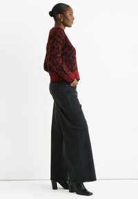 Red and black leopard print sweater with a ribbed hem, paired with high-waisted black wide-leg jeans and black heeled ankle boots.