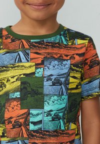 T-shirt met korte mouwen met een veelkleurige grafische print van voertuigen op een gestructureerde achtergrond, met groene accenten rond de halslijn.