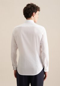 Camicia bianca a maniche lunghe con una texture liscia, dotata di un colletto standard, orlo arrotondato e polsini con bottoni. Design semplice e classico.