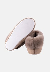 Pantofole in suede marrone con una morbida fodera in pelliccia, forma arrotondata e suola bianca imbottita. Dettaglio delle cuciture sul retro e texture morbida.