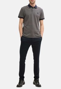 Polo shirt à motifs bleu marine et blanc avec un col, des manches courtes et un petit logo sur la poitrine, associé à un pantalon foncé ajusté et des chaussures noires.