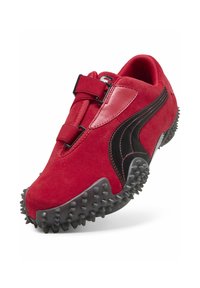 Punainen urheilukenkä, jossa musta logoraita, teksturoitu pohja piikeillä ja kaksi punaisen sävyistä säädettävää nauhaa kengän päällä.