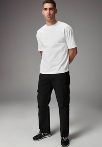 Hvid kortærmet t-shirt parret med sorte cargo bukser med sidelommer og lige ben-design, fuldendt med sorte sneakers.