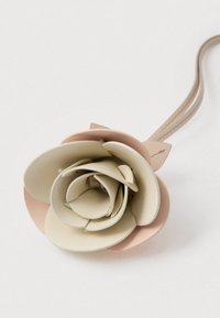 Krém- és finom rózsaszínű bőr virág kiegészítő. Réteges szirmokkal és vékony, bézs pánttal rögzítéshez. Simább felület, elegáns kivitel.