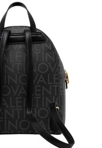 Mochila de cuero negro con patrón de logo en relieve, bolsillo con cremallera, asa superior y correas ajustables; forma estructurada y curva.