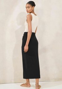Cream sleeveless bodysuit with a smooth texture, paired with a long black skirt featuring a draped design and gold flat sandals.