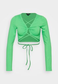 Zielony długi rękaw crop top wykonany z miękkiego materiału. Posiada detal w formie skrętu z wiązaniem na dolnym brzegu.