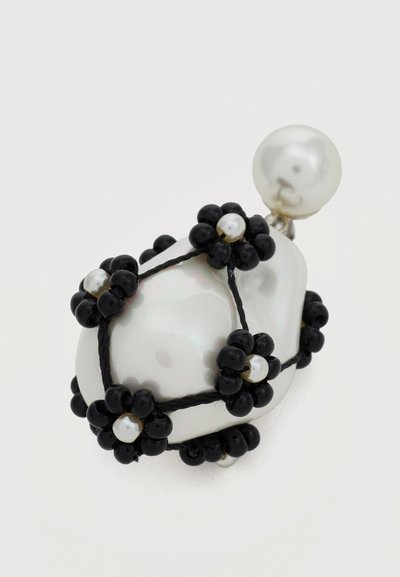 Boucle d'oreille en perle blanche irrégulière décorée de motifs floraux en perles noires et d'une petite puce en perle attachée.