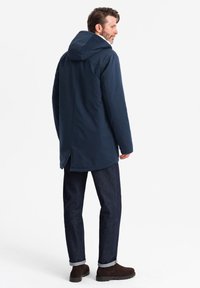Giacca a vento blu navale con una vestibilità rilassata, tessuto texturizzato e dettagli con apertura sul retro, abbinata a jeans in denim scuro e stivali in suede marrone.