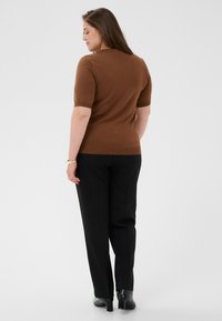 Pull marron à manches courtes avec une coupe ajustée, associé à un pantalon noir. La vue arrière du modèle montre une texture lisse et une silhouette simple.