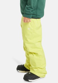 Jasné žlté snehové nohavice s hladkým povrchom, elastickým pásom a detailom loga. Čierne snehové topánky s gumovou podrážkou a bielymi akcentmi.