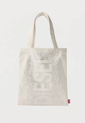 Bolsa de lona en color blanco roto con un gran texto "DIESEL" adornado con brillantes de strass y dos asas para el hombro. Etiqueta con el logo en rojo visible.