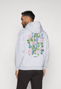 Hallhalline kapuutsviit, millel on lilleline muster, roosade lillede ja sinise kirjutisega "JUVENTUS" seljal. Pehme kangas ja ees asuv tasku.