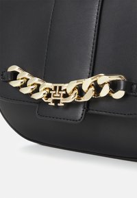 Borsa in pelle nera con dettaglio in catena dorata e logo. Texture liscia con linee pulite e una forma strutturata.