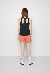 Czarny bezrękawnik z wycięciem na plecach, zestawiony z koralowymi szortami. Całość uzupełniają białe sportowe skarpetki i czarne buty.