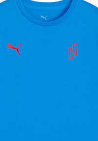 Blå crew neck t-shirt lavet af blødt stof, med et rødt Puma-logo på venstre bryst og et rødt "N"-design på højre side.